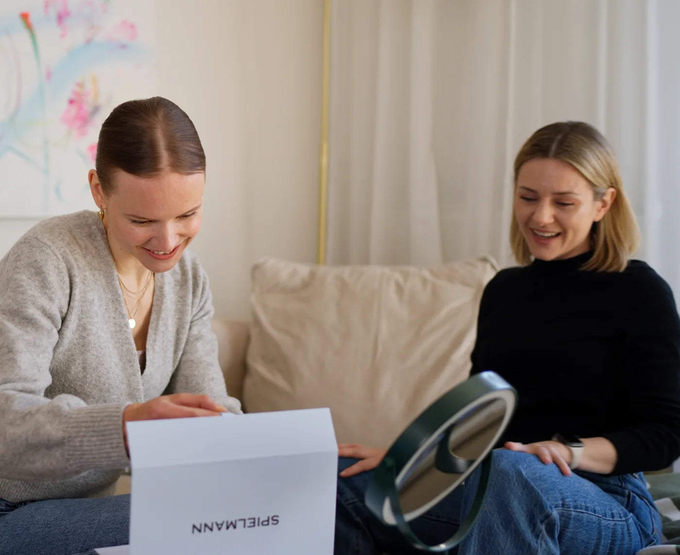 Zwei Frauen öffnen lachend auf dem Sofa ein Paket von Spielmann